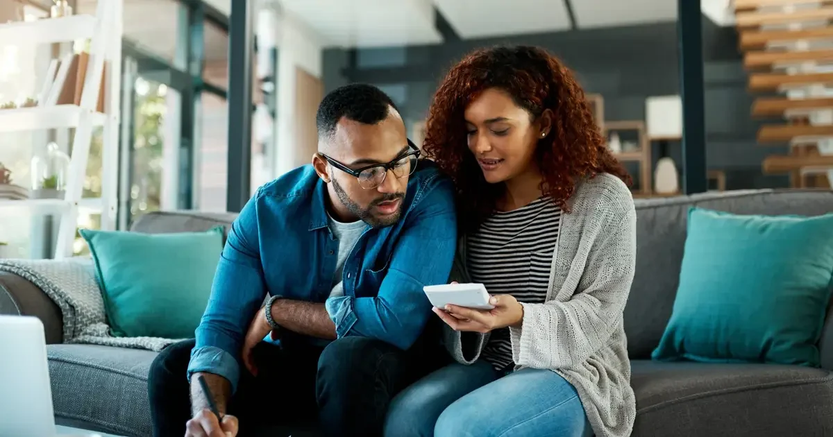 Couple reviews finances and smartphone together in modern living room