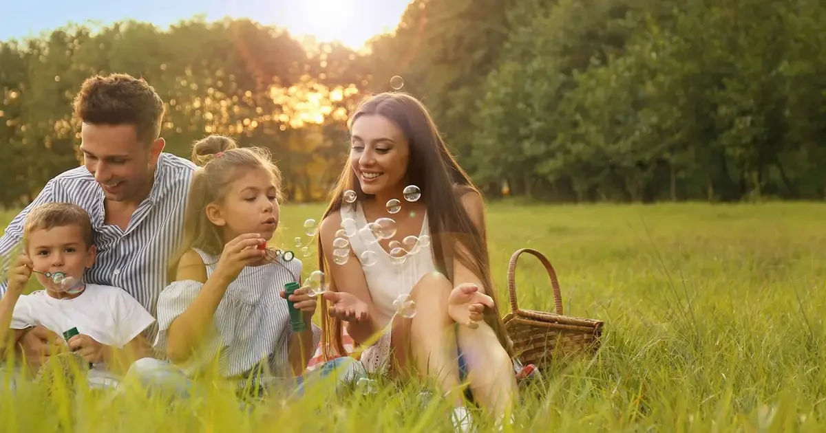 Family of four blowing bubbles in grass