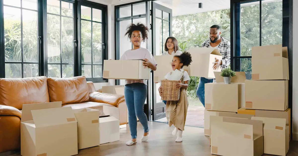 Joyful family carrying boxes into sunlit living room, smiling together.
