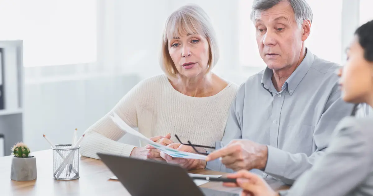 Older couple reviews documents with advisor in bright, modern office setting.